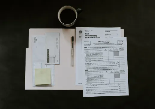 Tax documents, a pen, envelopes, sticky notes, and a mug of coffee are arranged on a dark surface, reflecting the focus needed when dealing with tasks like property line disputes.