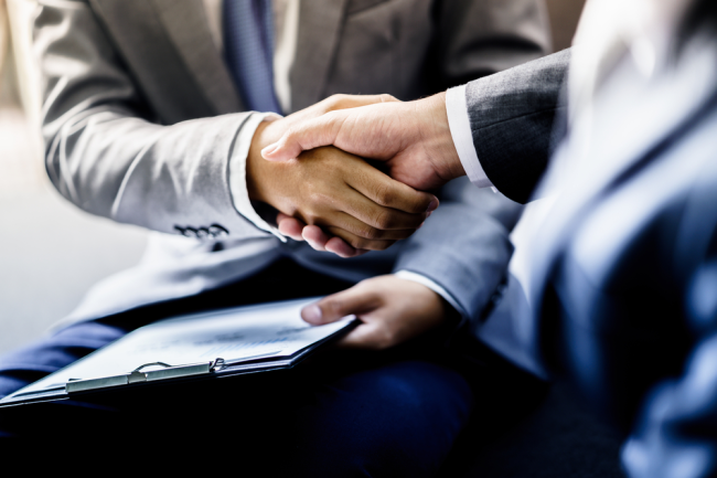 Two professionals in business attire shake hands, one holding a clipboard. The meeting's focus clearly revolves around resolving property line disputes with precision and professionalism.