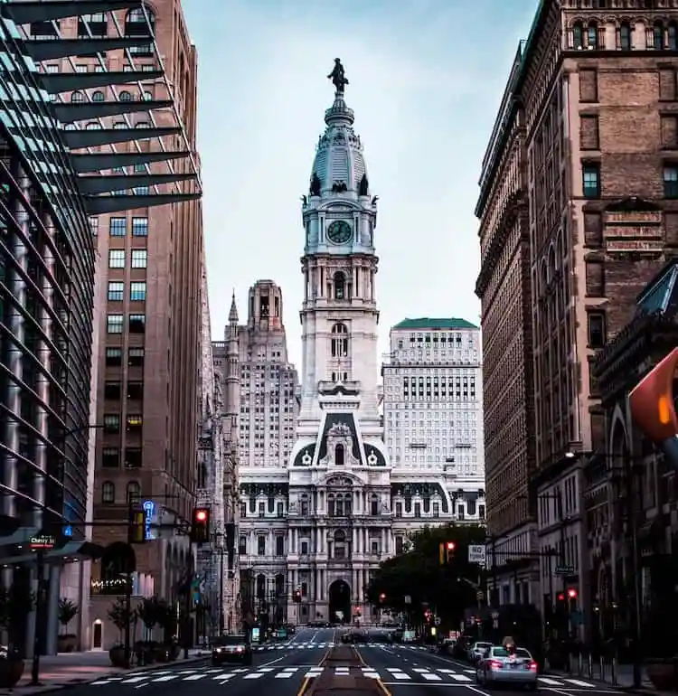 View of Philadelphia City Hall, featuring its iconic clock tower with a statue atop, flanked by tall buildings along an empty, wide street—a scene where history whispers and modern tales of property line disputes unfold.