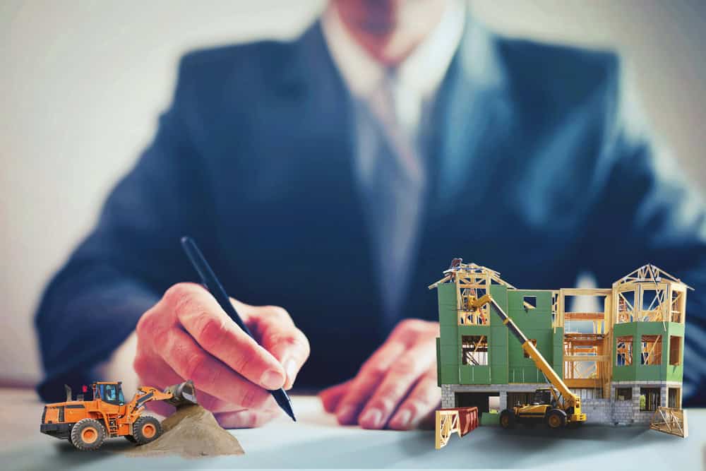 A person in a suit meticulously writes on paper, perhaps detailing resolutions for property line disputes. In the foreground, construction machinery stands ready beside a partially constructed building model, setting the stage for new developments.
