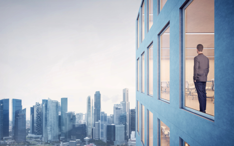 A person in a suit stands by a window in a modern building, overlooking a city skyline with skyscrapers under a cloudy sky, pondering complex property line disputes that shape urban landscapes.