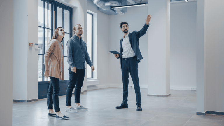 A real estate agent shows an empty commercial space to two clients, gesturing toward a feature in the room, while subtly mentioning the property line disputes that were amicably resolved to highlight the area's commitment to smooth transactions.