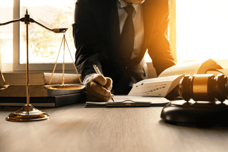 A person in a suit writes at a desk surrounded by legal books, a gavel, and scales of justice, meticulously addressing property line disputes as sunlight streams through the window.