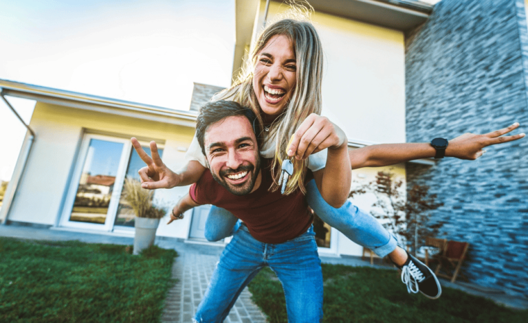 A joyful couple outside a modern house, blissfully unaware of any property line disputes; the woman holds a key while piggybacking on the man, both smiling.