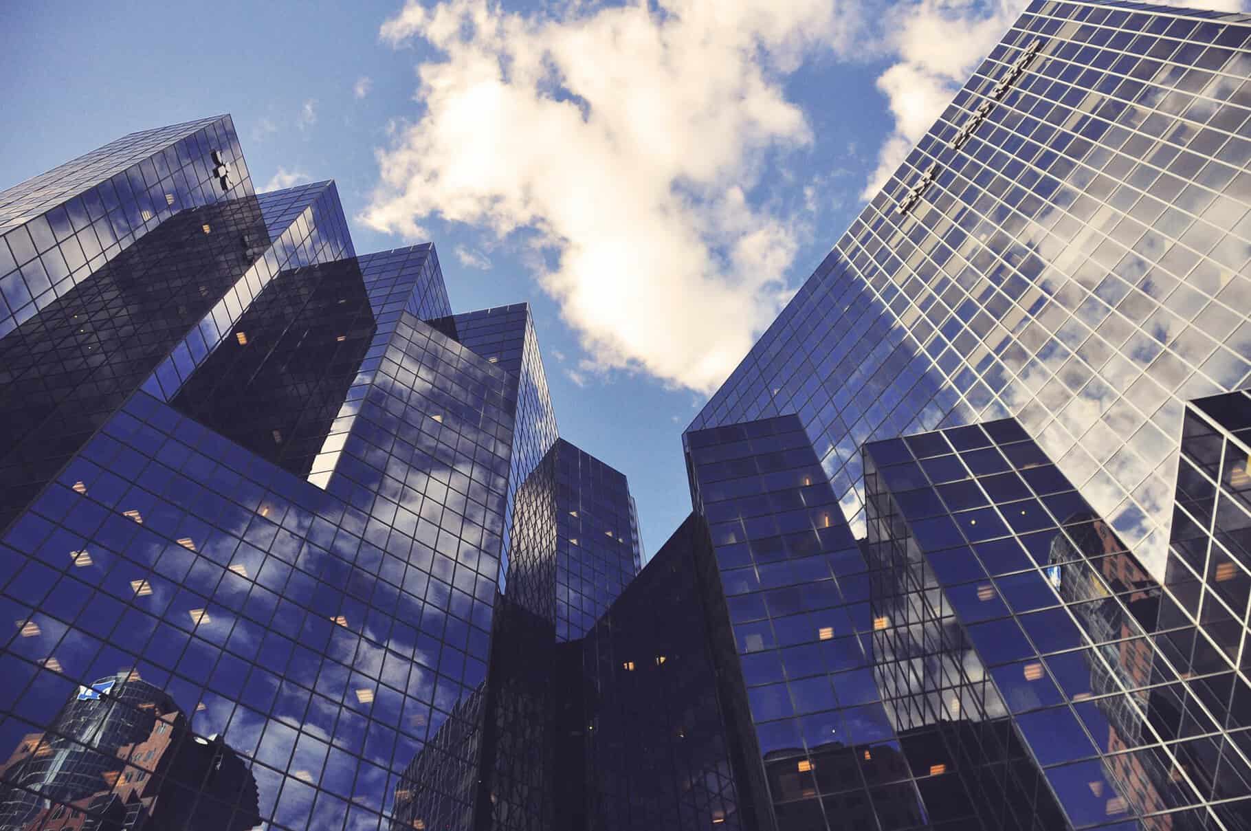 Tall glass skyscrapers reflecting clouds against a blue sky stand as reminders of modernity, where even property line disputes seem insignificant amid such towering elegance.