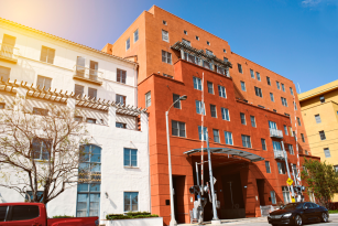 Street view of a mid-rise building with red and white facades under a clear blue sky, where parked cars and trees line the sidewalk, highlighting the peaceful setting despite occasional property line disputes.