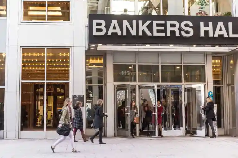 People walking in front of the entrance to Bankers Hall, a commercial building with large glass windows and revolving doors, mindful of property line disputes in this bustling district.