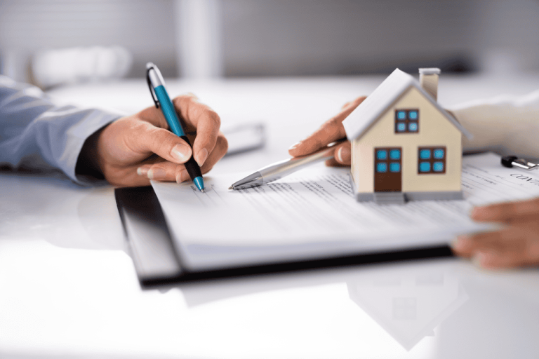 Two hands holding pens hover over a contract, carefully outlining terms, as a small house model sits on the table—a silent witness to potential property line disputes.