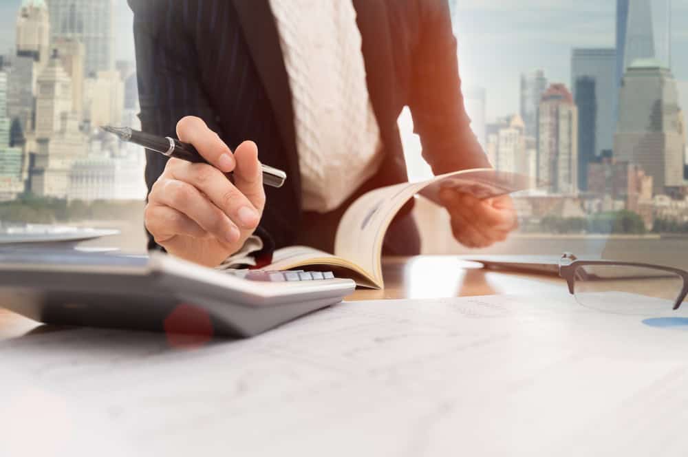 A person in a suit is working at a desk laden with papers, pen in hand, navigating through property line disputes. The city skyline serves as a distant backdrop to the focused determination on their face.