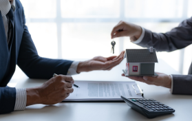 A person hands over keys to another holding a model house, while a contract and calculator sit on the table. Amidst this transaction, whispers of property line disputes linger in their minds, hinting at complexities beyond the paperwork.