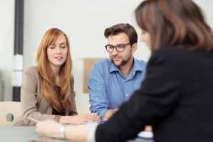 Three people engaged in a discussion at a table in an office setting. One person faces away, while the other two sit side by side, listening intently to unravel the complexities of property line disputes.