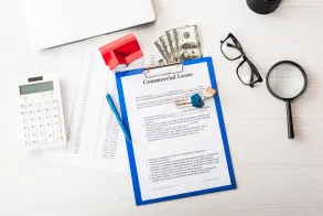 A commercial lease document on a clipboard rests on a desk alongside tools of financial negotiation: calculator, glasses, magnifying glass, cash, pen, red stamp, papers, and laptop—poised for clarity in complex matters like property line disputes.