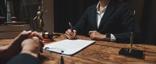 Lawyer advising client while reviewing documents and writing notes at desk