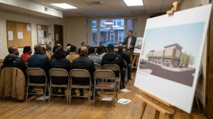 speaker presenting building rendering on easel to seated community meeting attendees